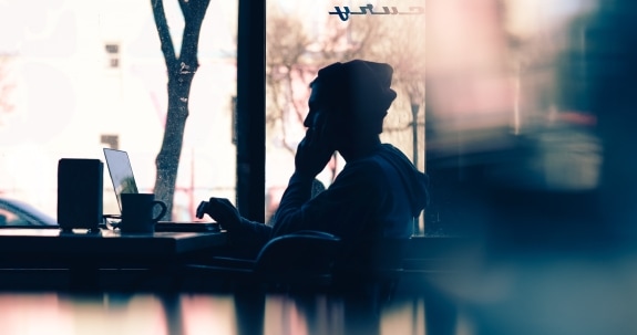 Silhouette of a person sitting at a table with a laptop