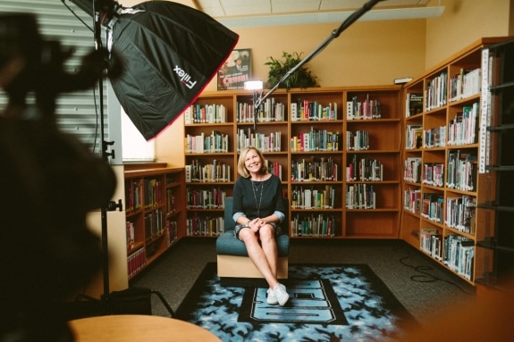 Woman sitting on chair in front of bookshelves talking in an interview