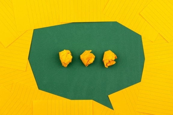 Three scrunched balls of yellow paper on green surface surrounded by yellow lined paper